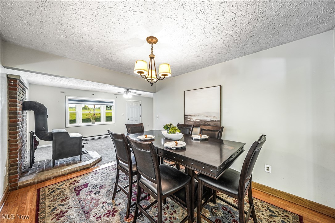 6916 Dewey Road Thompson, OH 44086 - Photo 5 of 49 Dining area with wood finished floors, a textured ceiling, a chandelier, a ceiling fan, and a baseboard heating unit