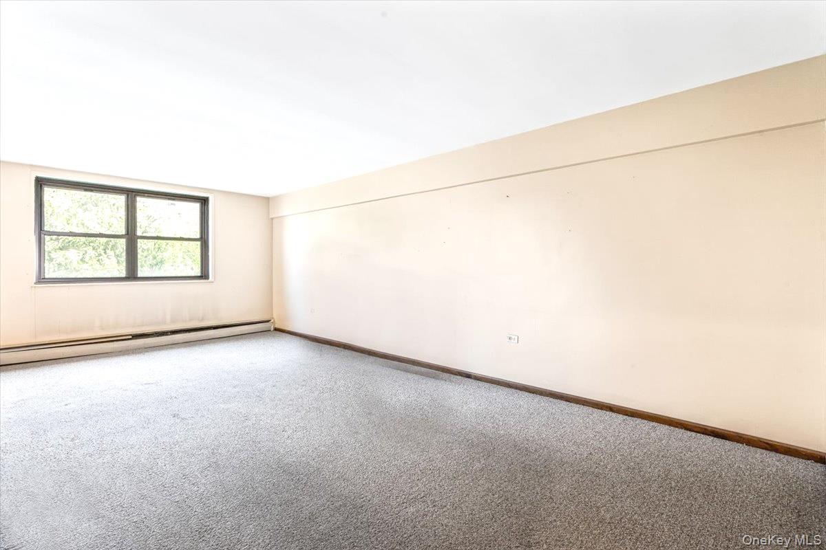 99-35 59th Avenue, Unit L5 Queens, NY 11368 - Photo 3 of 17 Carpeted empty room featuring a baseboard heating unit and baseboards