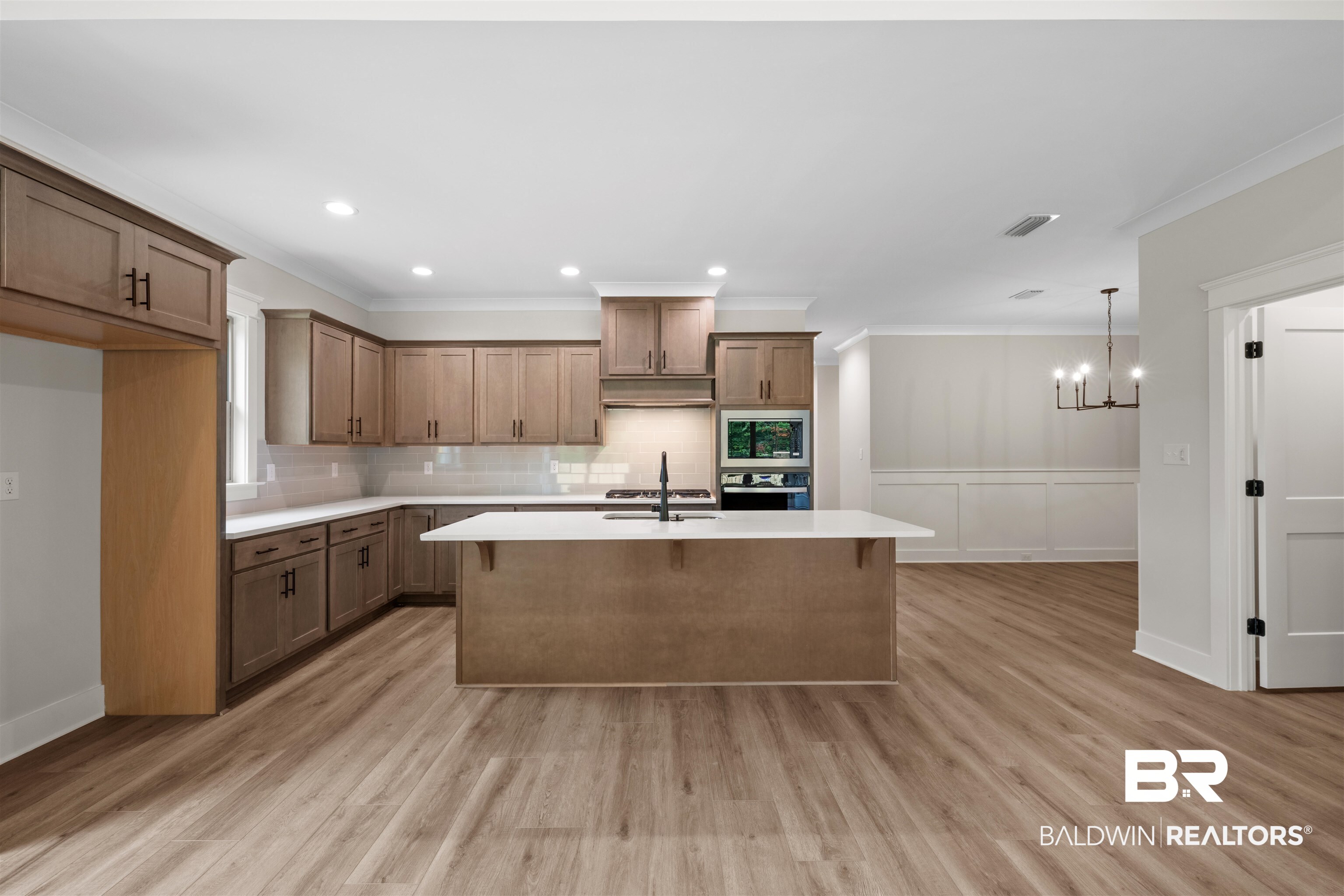 27494 Patch Pl Loop Daphne, AL 36526 - Photo 9 of 26 Modern kitchen featuring L-shaped cabinetry, a central island with a sink, built-in wall oven and microwave, light wood-finish flooring, and crown molding
