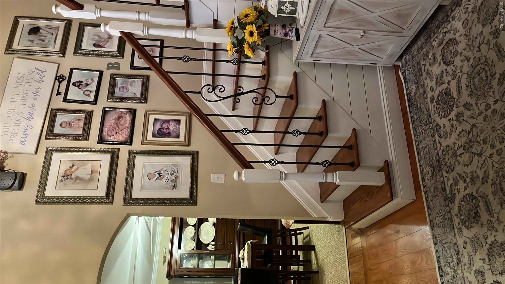 124 Rutsonville Road Wallkill, NY 12589 - Photo 21 of 33 Hardwood flooring at the base of a staircase featuring wood treads, white risers, and black iron balusters with decorative elements.