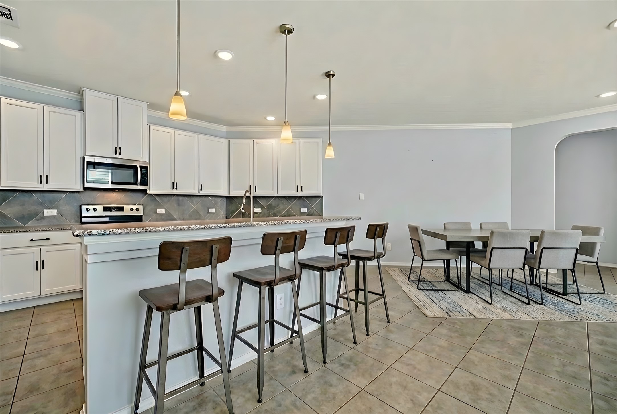 13917 Inaugural Street Manor, TX 78653 - Photo 10 of 39 Kitchen featuring decorative light fixtures, crown molding, stainless steel microwave, a breakfast bar area, and white cabinetry