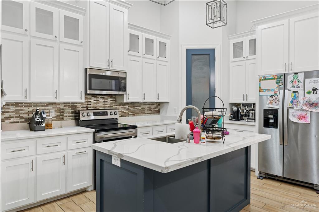 311 Seguin Loop Rio Grande City, TX 78582 - Photo 5 of 15 White shaker-style cabinetry, a contrasting island with a countertop, stainless steel appliances, and a mosaic tile backsplash