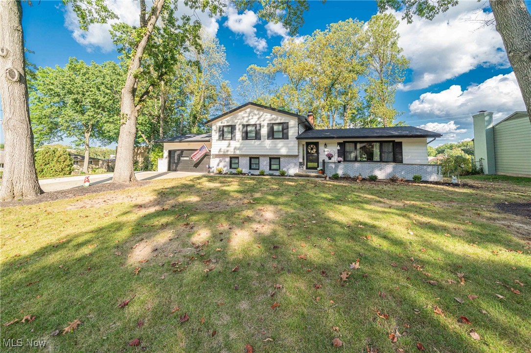 Tri-level home with a chimney, brick siding, a front lawn, and concrete driveway