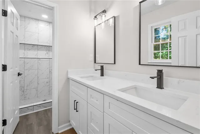 a bathroom with double vanity sink a two mirror a window and a glass door shower
