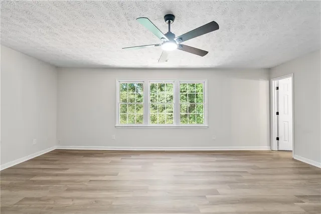 an empty room with wooden floor fan and windows