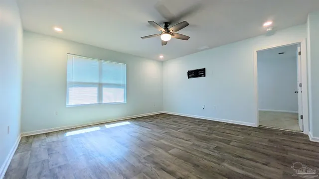an empty room with wooden floor chandelier fan and windows
