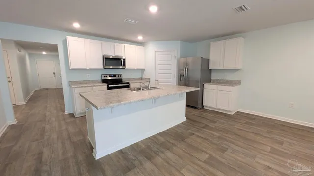 a kitchen with stainless steel appliances a stove top oven a sink a refrigerator white cabinets and wooden floor