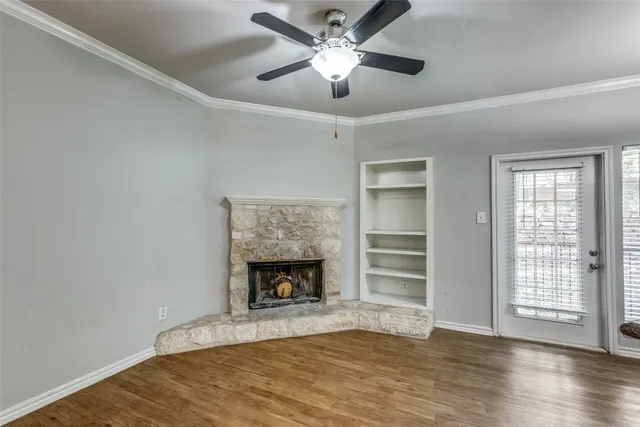 a view of an empty room with a fireplace a ceiling fan and wooden floor