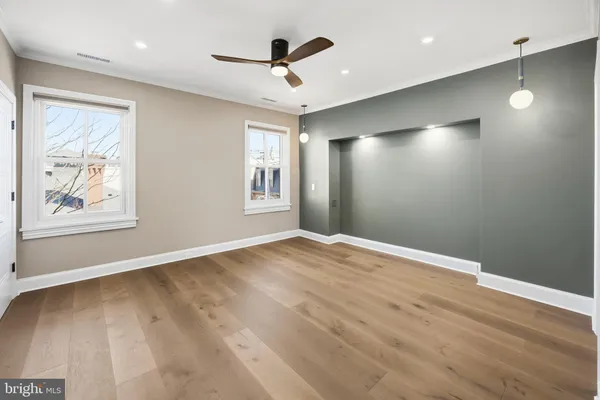 a view of an empty room with wooden floor and a ceiling fan