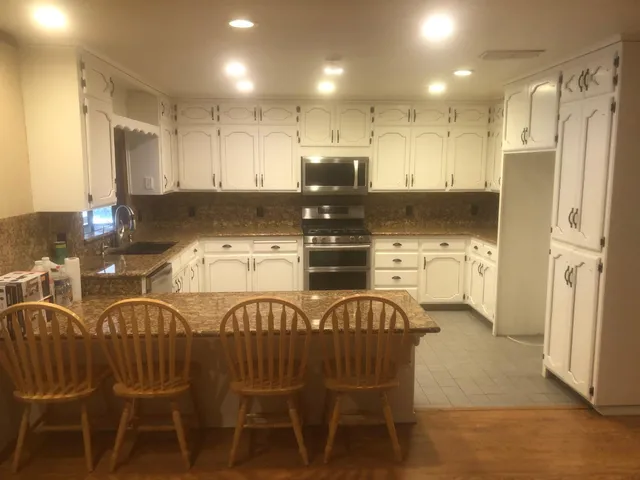 a kitchen with stainless steel appliances granite countertop a dining table chairs refrigerator and sink