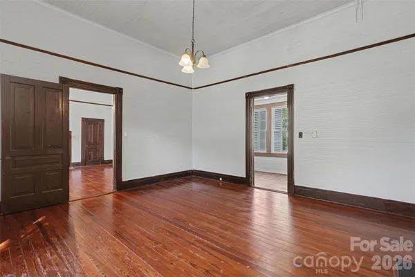 an empty room with wooden floor chandelier and windows