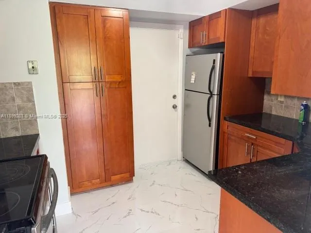 a view of a refrigerator in kitchen and an empty room with wooden floor
