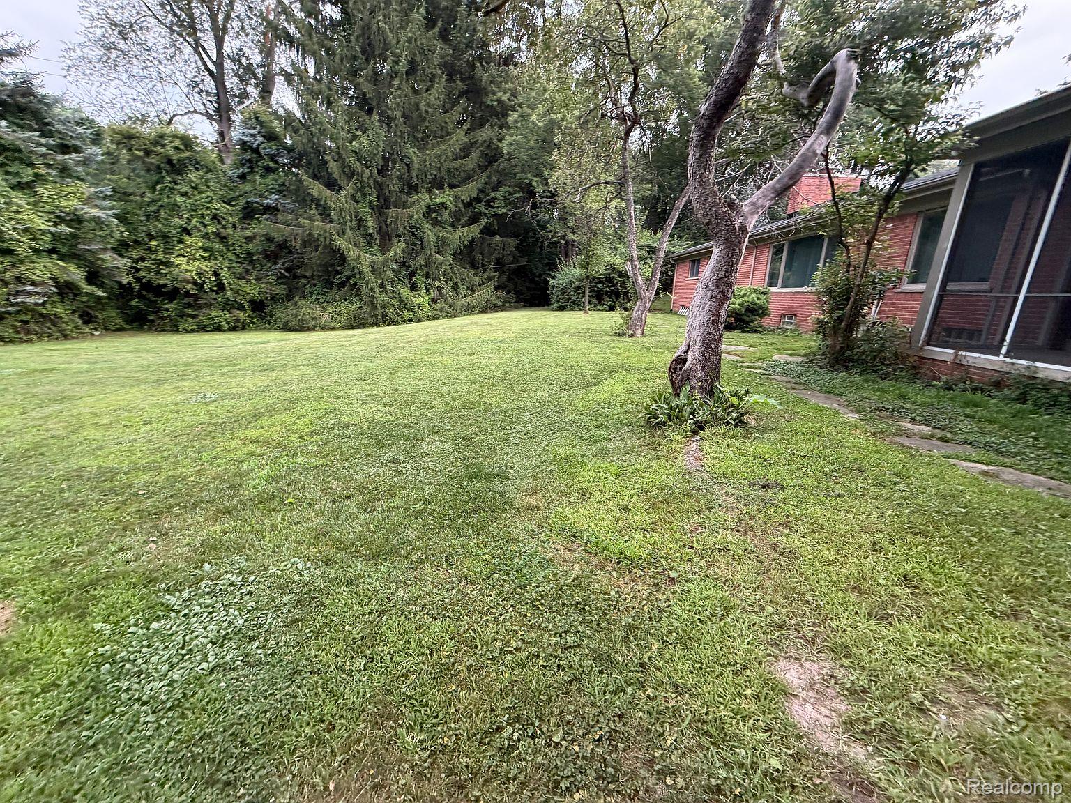 3520 Rayburn Road Bloomfield Hills, MI 48304 - Photo 7 of 26 Expansive lawn with mature trees and dense perimeter foliage, featuring a brick exterior and a screened-in porch