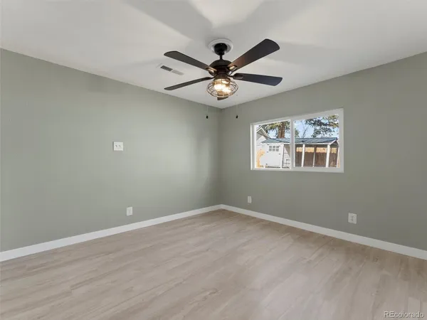 an empty room with wooden floor ceiling fan and window