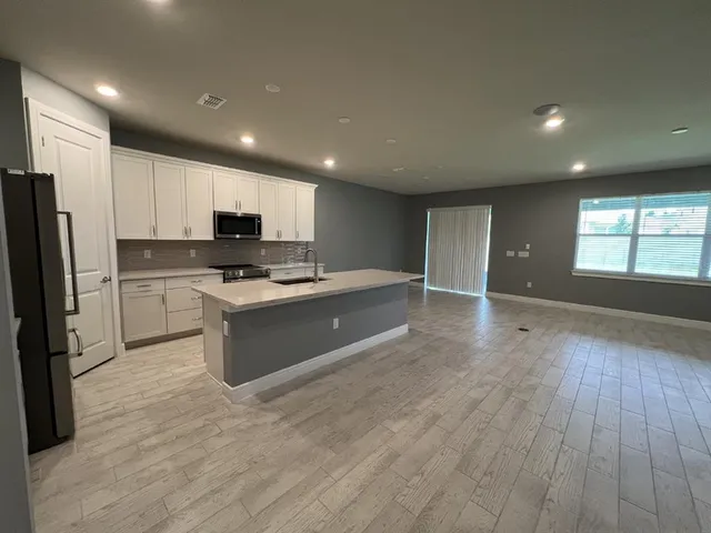 a large kitchen with stainless steel appliances a large counter top a stove a refrigerator cabinets and a wooden floor