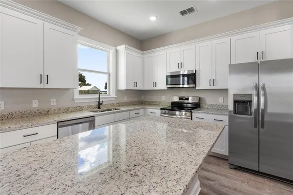 a large kitchen with granite countertop a stove a sink a refrigerator and white cabinets