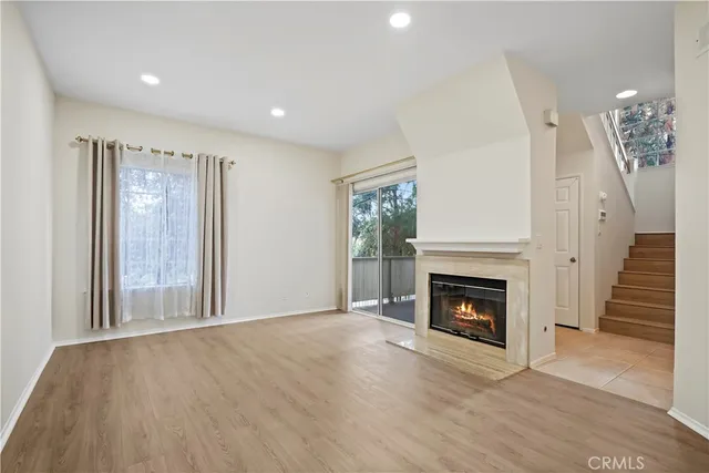 a view of an empty room with wooden floor fireplace and a window