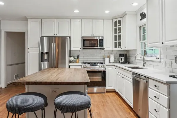 a kitchen with stainless steel appliances granite countertop a stove a sink a microwave a refrigerator and white cabinets