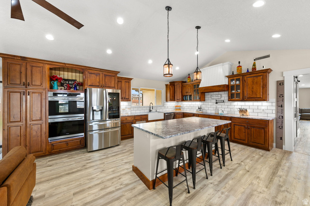2591 East Washington Dam Road Washington, UT 84780 - Photo 11 of 67 Spacious kitchen featuring an expansive center island with seating, wood-finish flooring, stainless steel appliances, white subway tile backsplash, and rich wood cabinetry