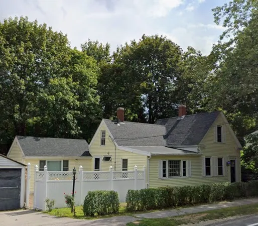 a view of a white house next to a yard with plants and trees