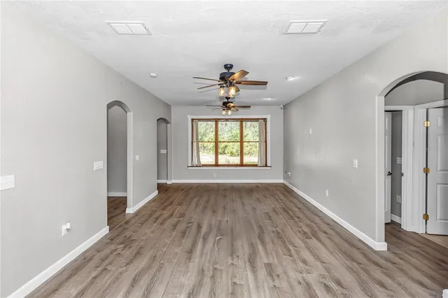 an empty room with wooden floor chandelier fan and windows