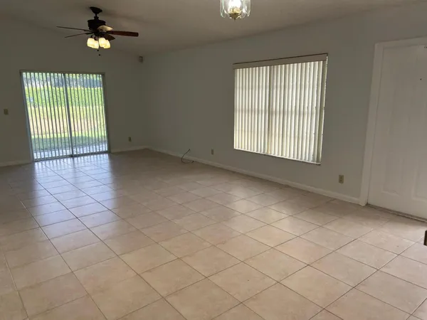 an empty room with chandelier fan and windows