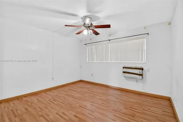 a view of an empty room with wooden floor and a ceiling fan