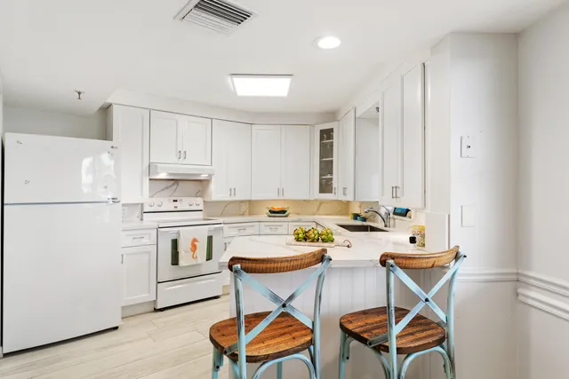 a kitchen with stainless steel appliances kitchen island granite countertop a refrigerator a stove a sink and white cabinets with wooden floor