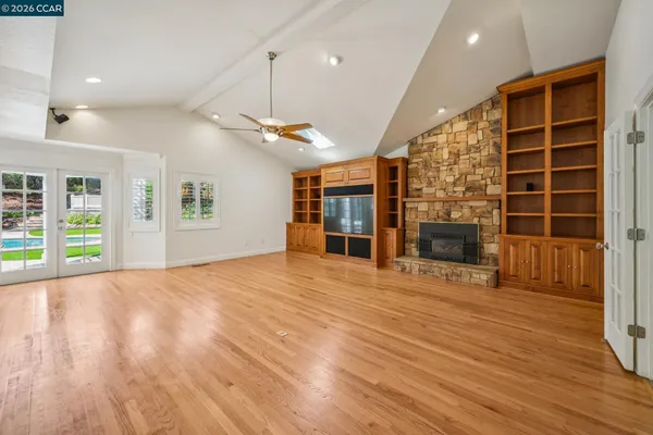 a view of an empty room and kitchen with wooden floor
