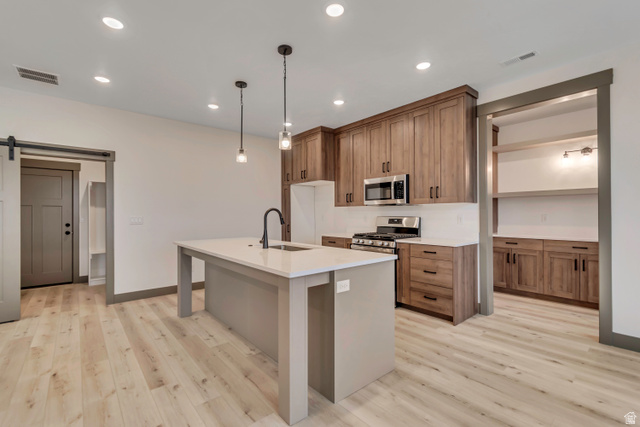 3317 South 1000 West, Unit 6010 Logan, UT 84321 - Photo 18 of 34 Kitchen featuring a barn door, a kitchen island with sink, stainless steel appliances, hanging light fixtures, and light wood-style flooring