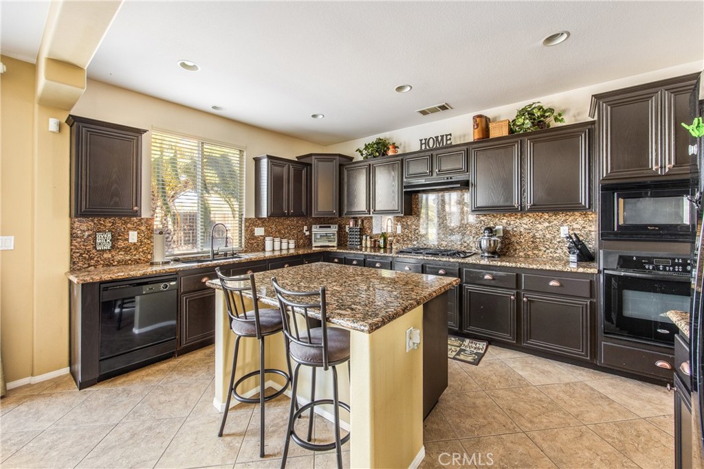 18936 Malkoha Street Perris, CA 92570 - Photo 17 of 70 a kitchen with stainless steel appliances granite countertop a stove top oven a sink dishwasher a dining table and chairs with wooden floor