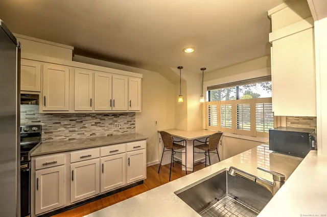 a kitchen with stainless steel appliances granite countertop a stove a sink and white cabinets with wooden floor