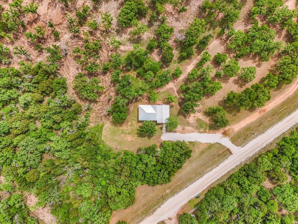 304 County Road 340 Ranger, TX 76470 - Photo 16 of 30 Expansive wooded lot featuring a single-story structure with a light-colored roof, a gravel driveway, and surrounding natural vegetation