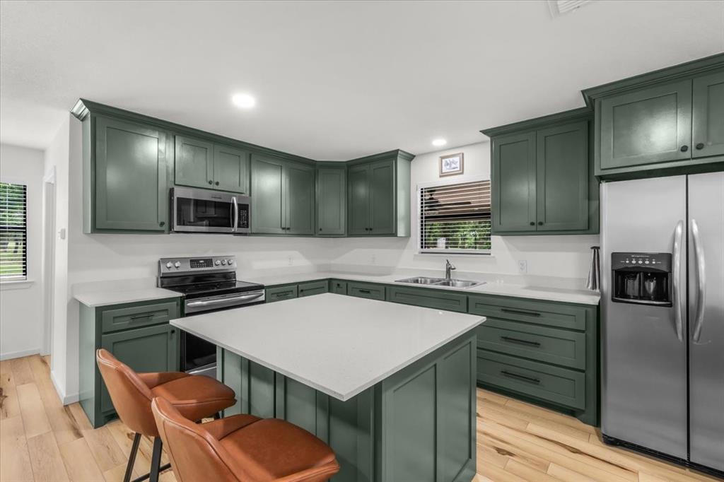 304 County Road 340 Ranger, TX 76470 - Photo 5 of 30 Kitchen featuring green cabinetry with dark hardware, white countertops, stainless steel appliances, and wood-finish flooring