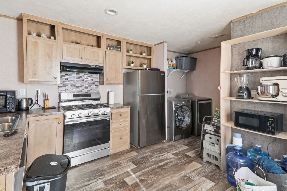 Kitchen featuring light brown cabinetry, stainless steel appliances, under cabinet range hood, open shelves, and dark wood-style flooring