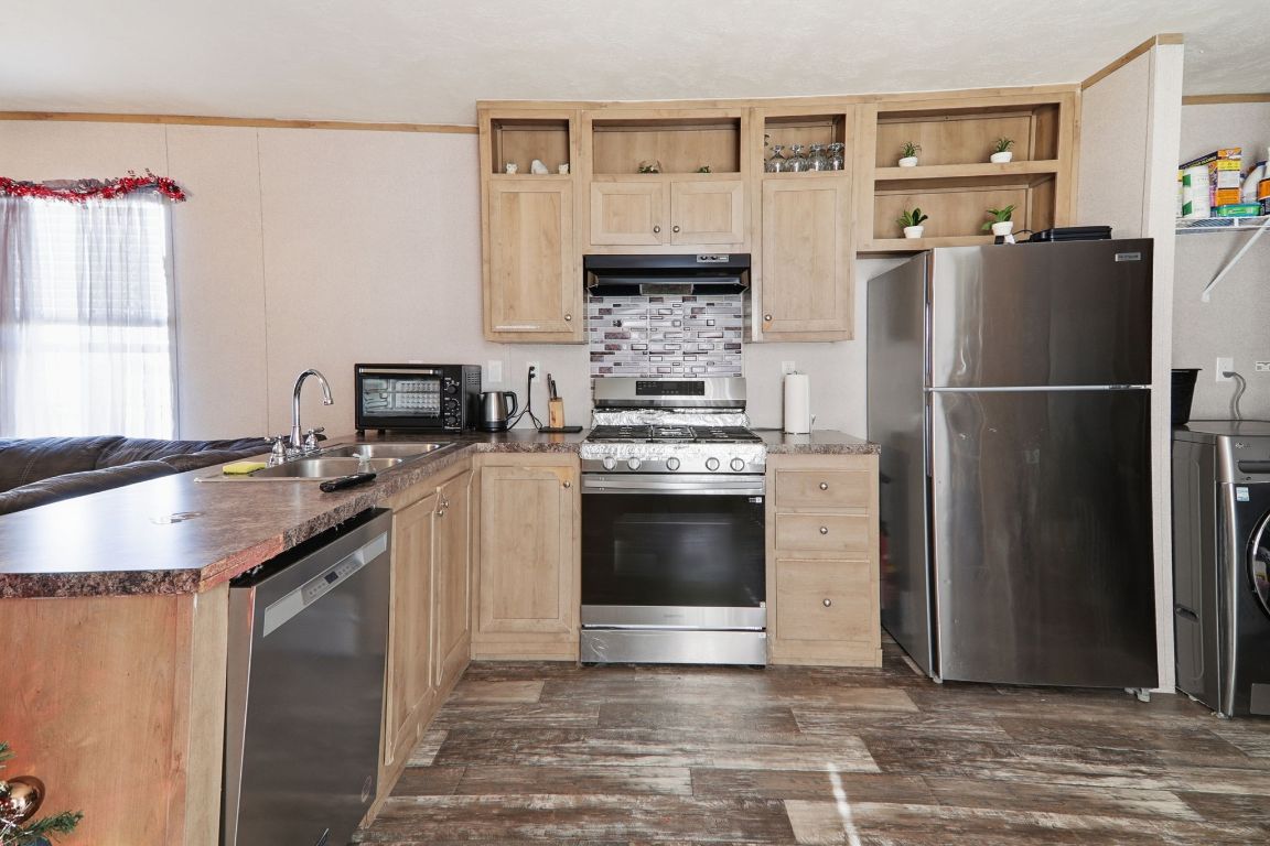 1130 Rustler Pass Kyle, TX 78640 - Photo 6 of 21 Kitchen with crown molding, light brown cabinetry, appliances with stainless steel finishes, washer / clothes dryer, and a peninsula
