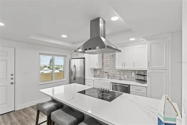 a large kitchen with kitchen island a stove a sink a refrigerator and white cabinets with wooden floor