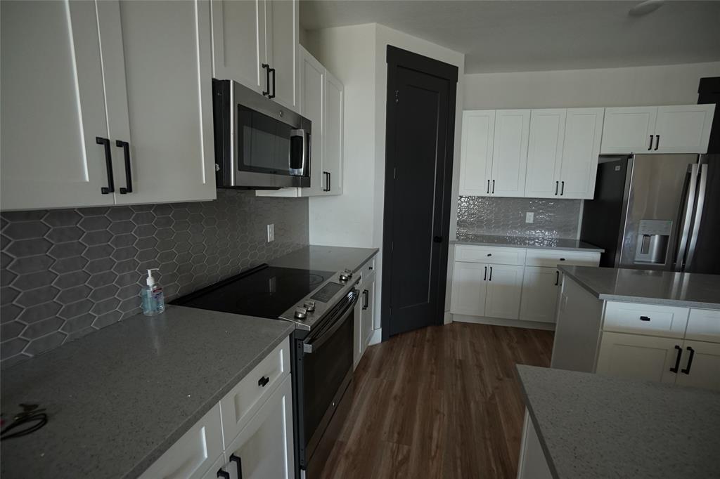 1764 Palladio Loop Princeton, TX 75407 - Photo 7 of 40 Modern kitchen featuring white cabinetry, stainless steel appliances, grey composite countertops, a hexagonal tile backsplash, and wood-finish flooring