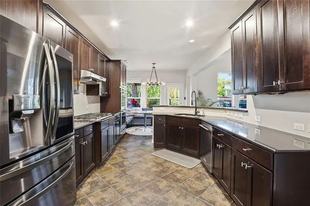a large kitchen with stainless steel appliances wooden cabinets a stove top oven a sink and dishwasher