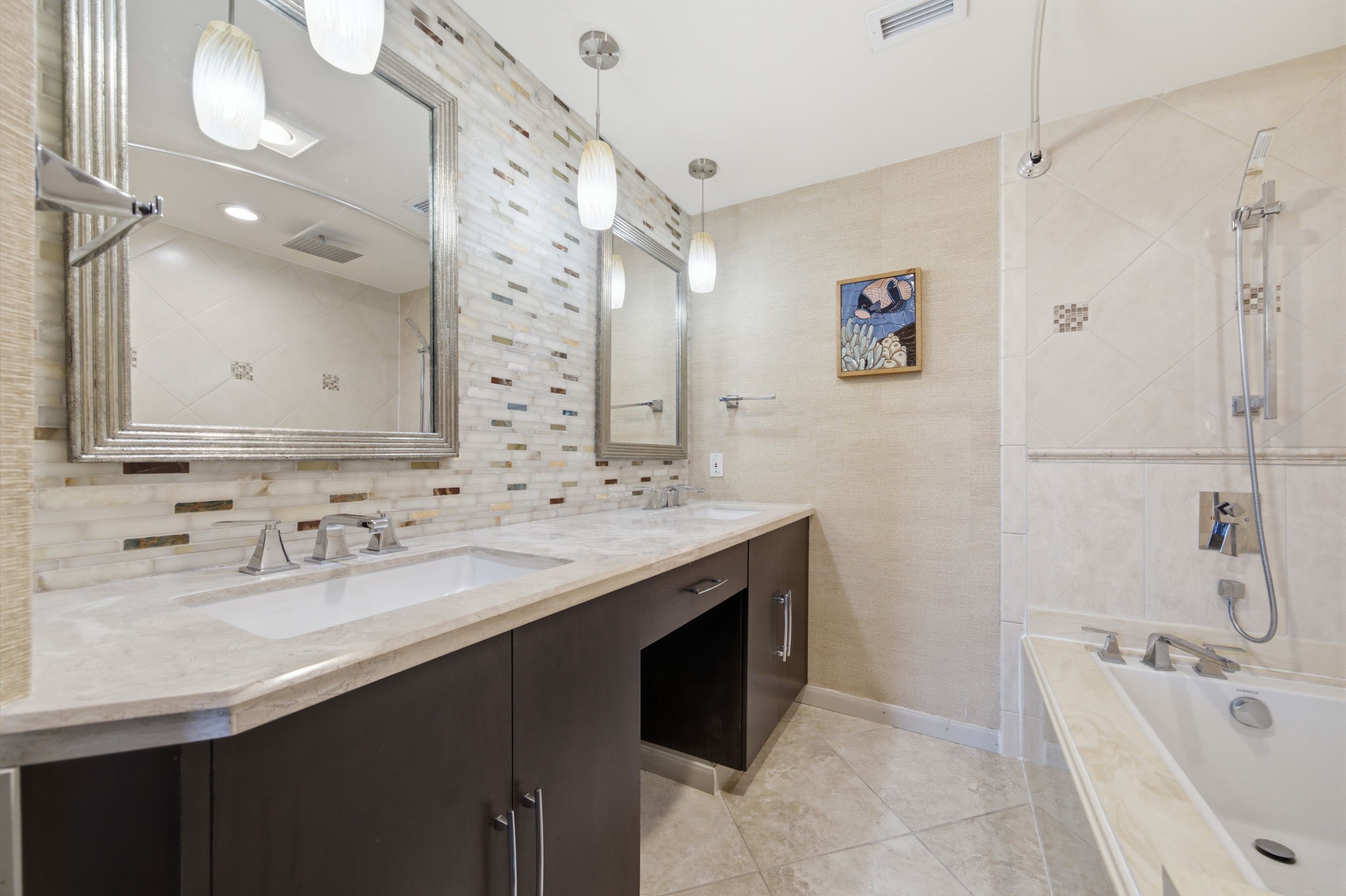 3350 McCue Road, Unit 2402 Houston, TX 77056 - Photo 37 of 49 A mosaic-tiled accent wall and dual hanging pendant lights elevate this secondary bath, highlighting an extended dark wood vanity with a knee space. Polished stone countertops, framed mirrors, and an adjacent soaking tub with a handheld sprayer create a refined space for guests.