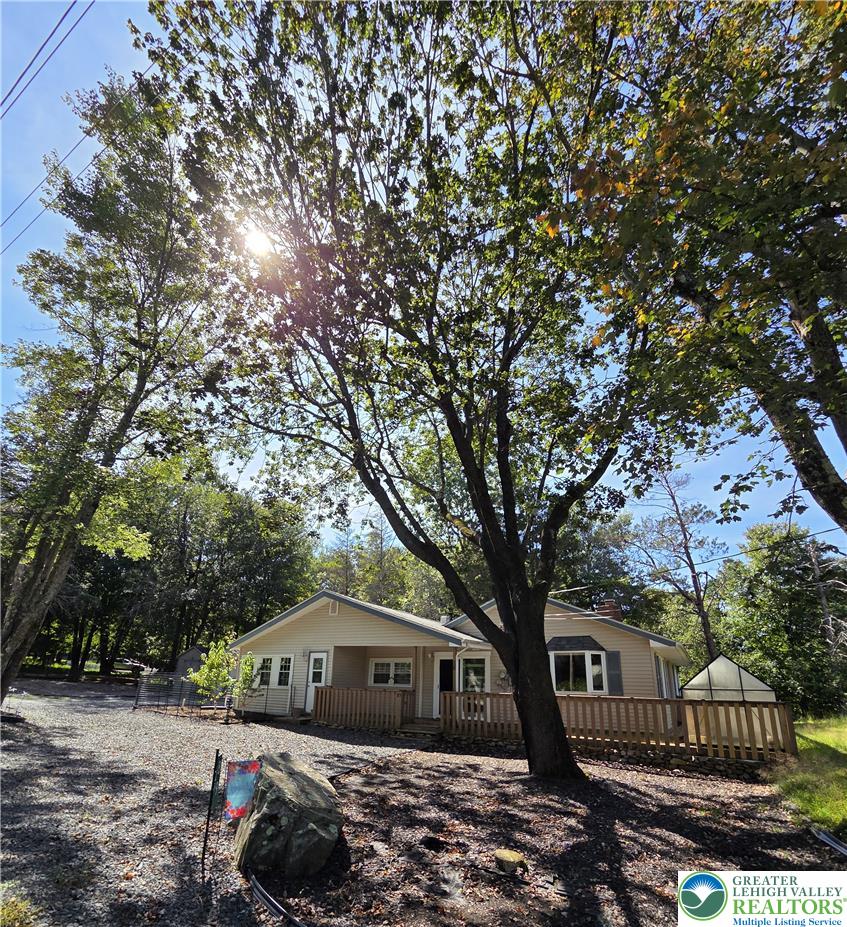 Mature trees shade a welcoming front deck in a peaceful wooded setting.