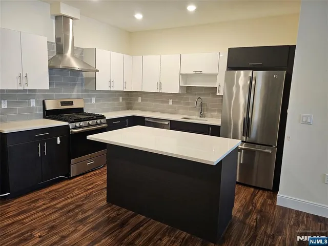 a kitchen with stainless steel appliances a sink dishwasher a refrigerator a stove and white cabinets with wooden floor