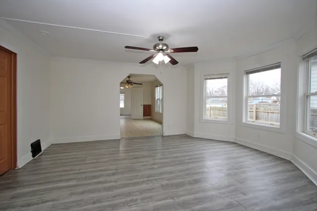an empty room with wooden floor chandelier fan and windows