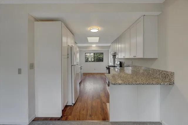 a kitchen with stainless steel appliances granite countertop a stove a sink dishwasher a refrigerator white cabinets and wooden floor