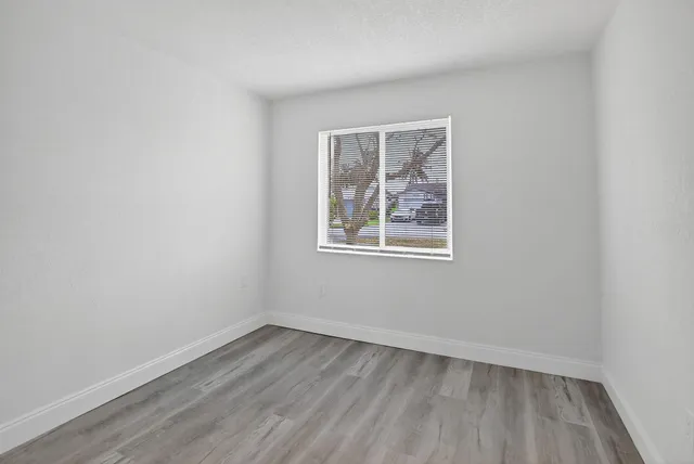 a view of an empty room with wooden floor and a window