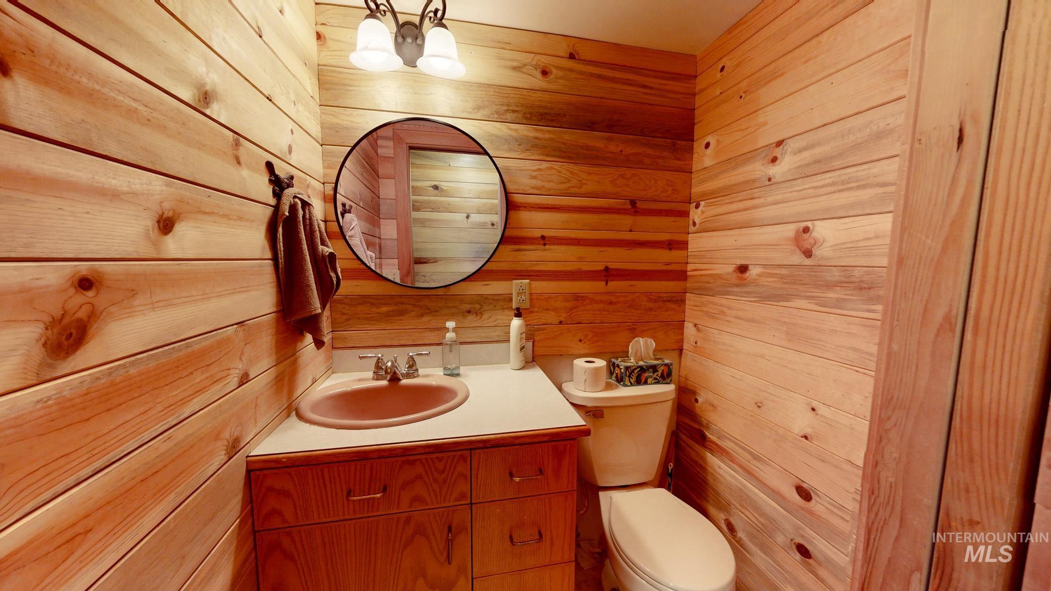 863 Pottery Road Bliss, ID 83314 - Photo 7 of 45 Wood-paneled bathroom featuring a vanity with a drop-in sink, wall-mounted light fixture, and a circular mirror