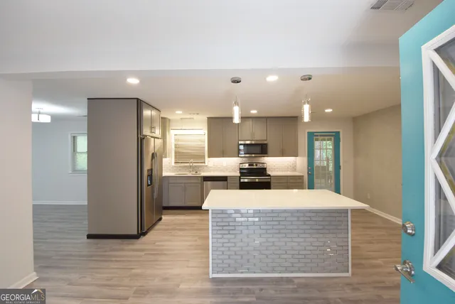 a kitchen with kitchen island a stove a refrigerator a sink a dining table and chairs with wooden floor