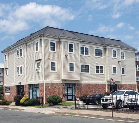a front view of a building with lot of cars and trees
