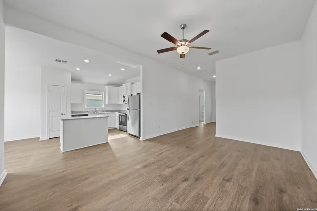 a view of an empty room and kitchen with wooden floor sink