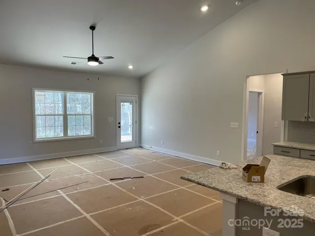 a view of an empty room with kitchen and window